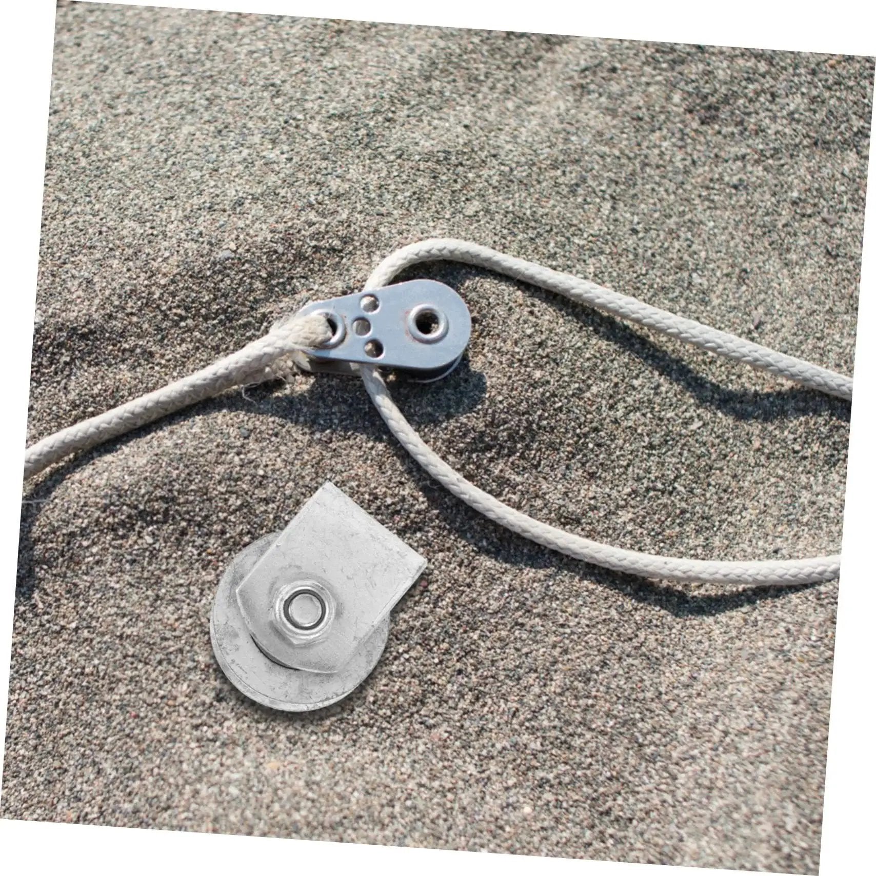 Metal pulley and rope system on sandy surface, showcasing components used in industrial cast iron groove wheel garage door roller setups.