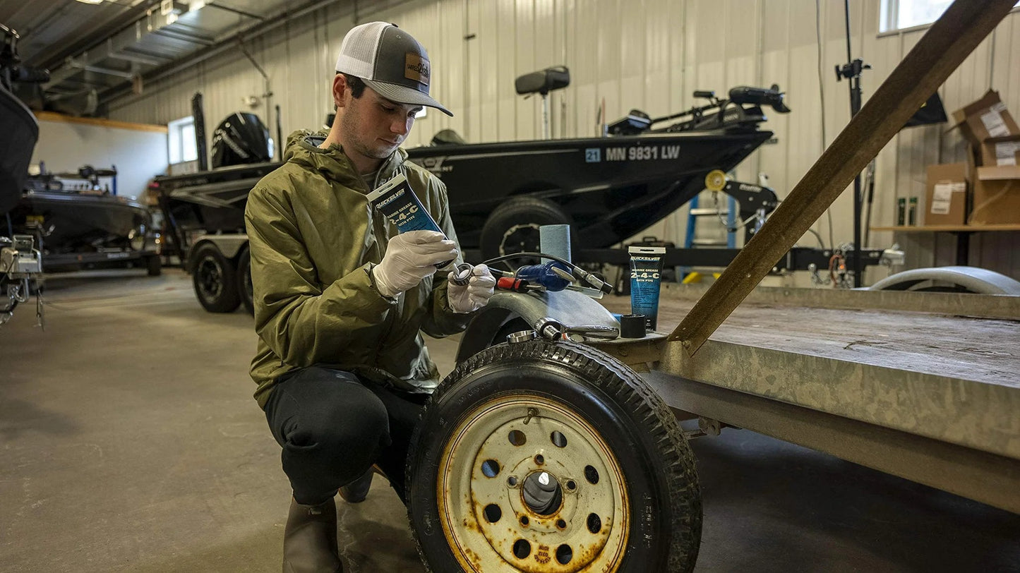 Person applying 2-4-C Marine Grease With PTFE Teflon For Boats And Cables on trailer wheel in garage