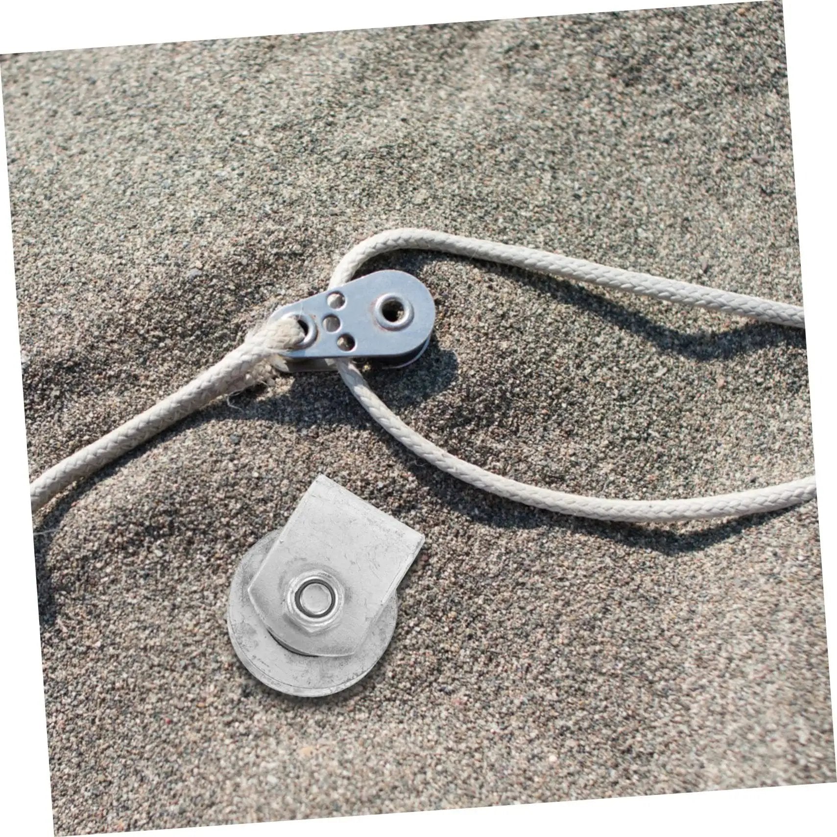 Cast Iron V-Groove Wheel Heavy Duty Steel Roller beside a rope on sandy ground, showcasing the wheel's durable design and utility.