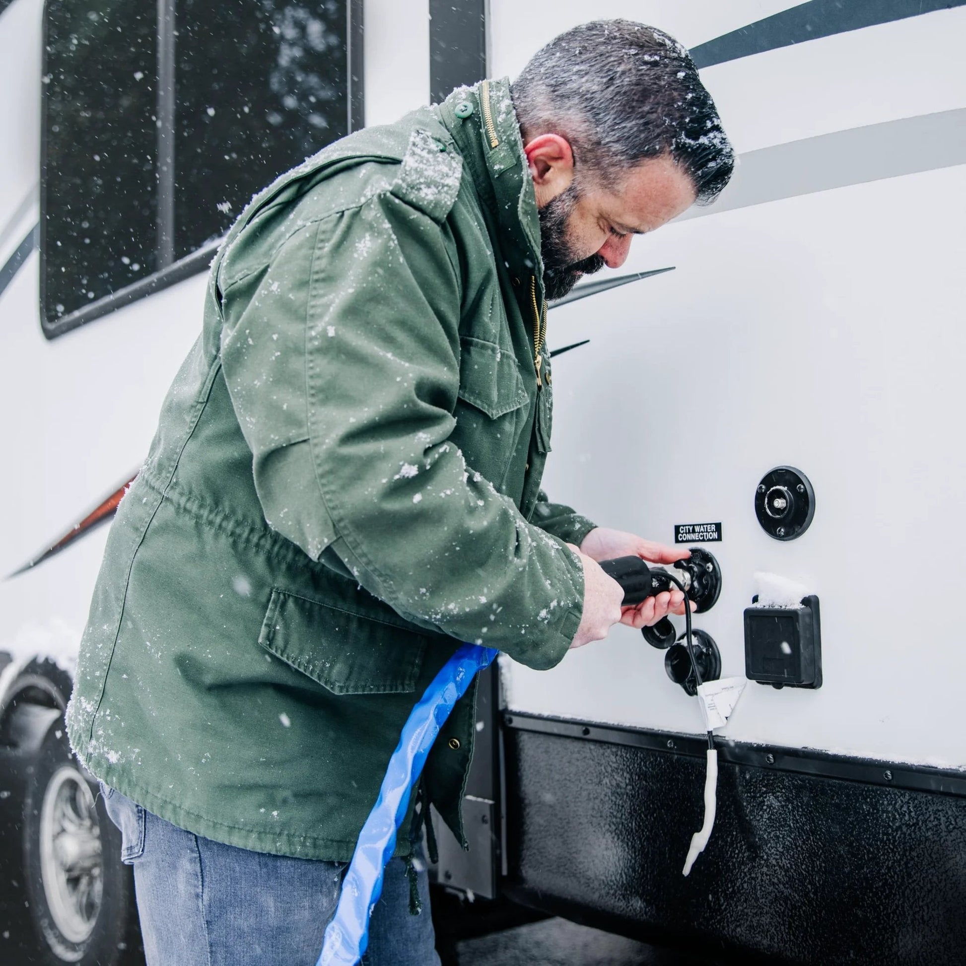 Man connecting Heated RV Water Hose With Freeze Protection To Minus 20 Degrees Fahrenheit For All Weather Use Premium NSF 61 Drinking Water Hose Lead Free BPA Free Phthalate Free With Energy Saving Thermostat And Adapter For Connection To Either End Of Hose to an RV in snowy conditions