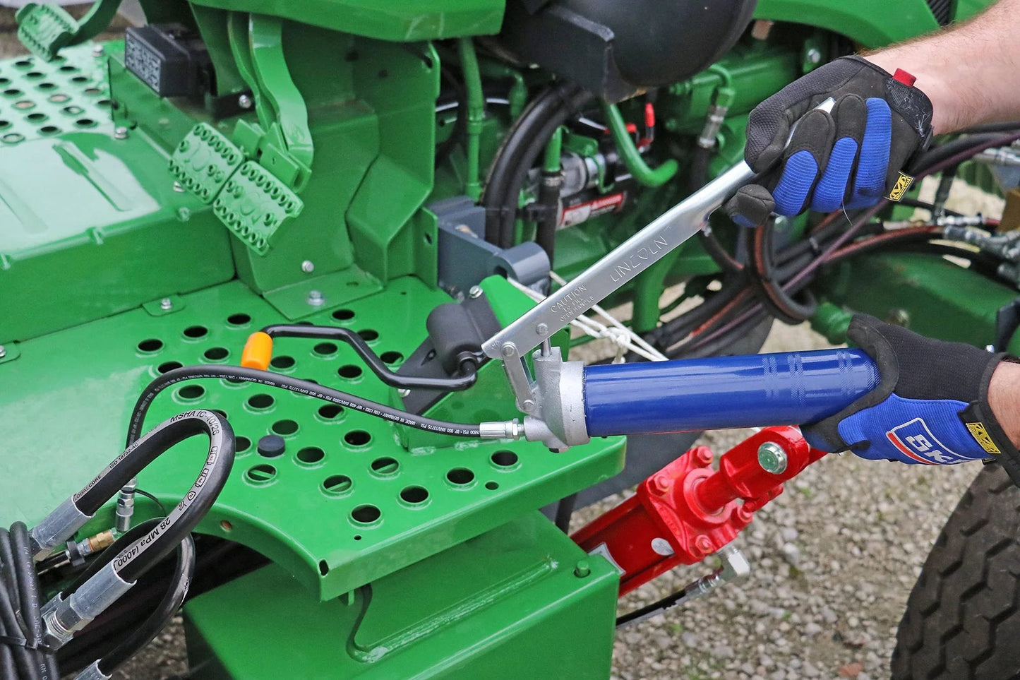Person using Heavy Duty Lever Action Grease Gun With 18 Inch Whip Hose And Coupler, Jam Proof Toggle on farm machinery