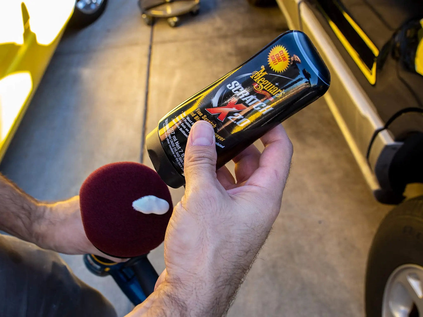 Meguiars ScratchX 2.0 G10307C scratch remover for car paint held by a person in a garage setting.