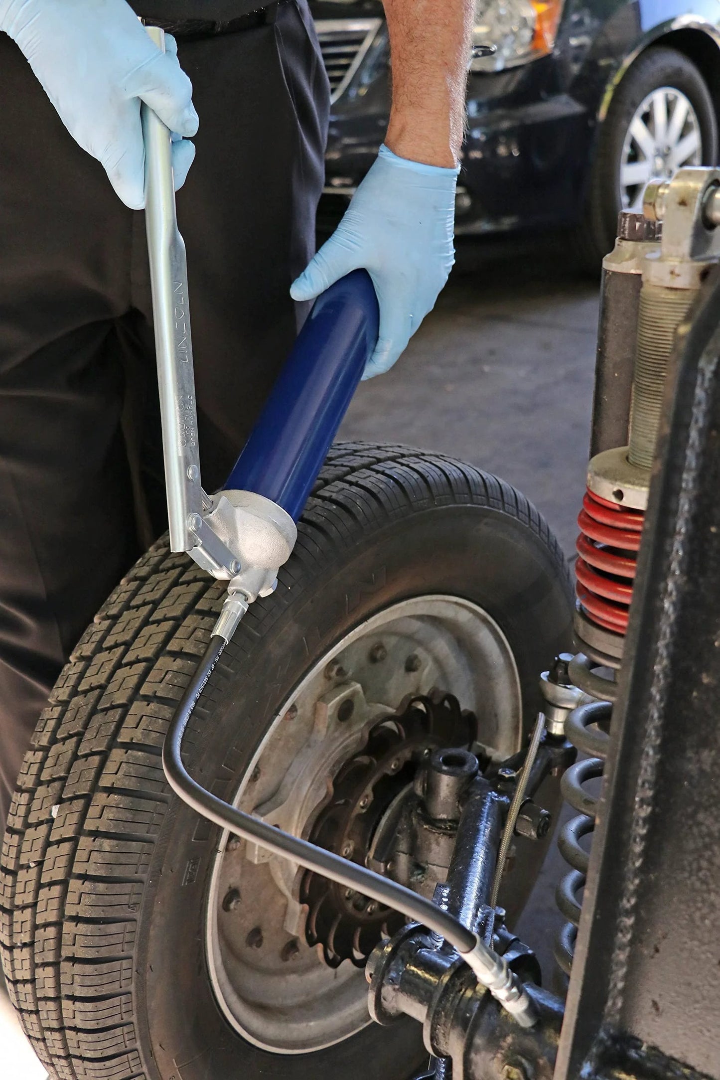 Person using Heavy Duty Lever Action Grease Gun With 18 Inch Whip Hose And Coupler, Jam Proof Toggle on vehicle wheel