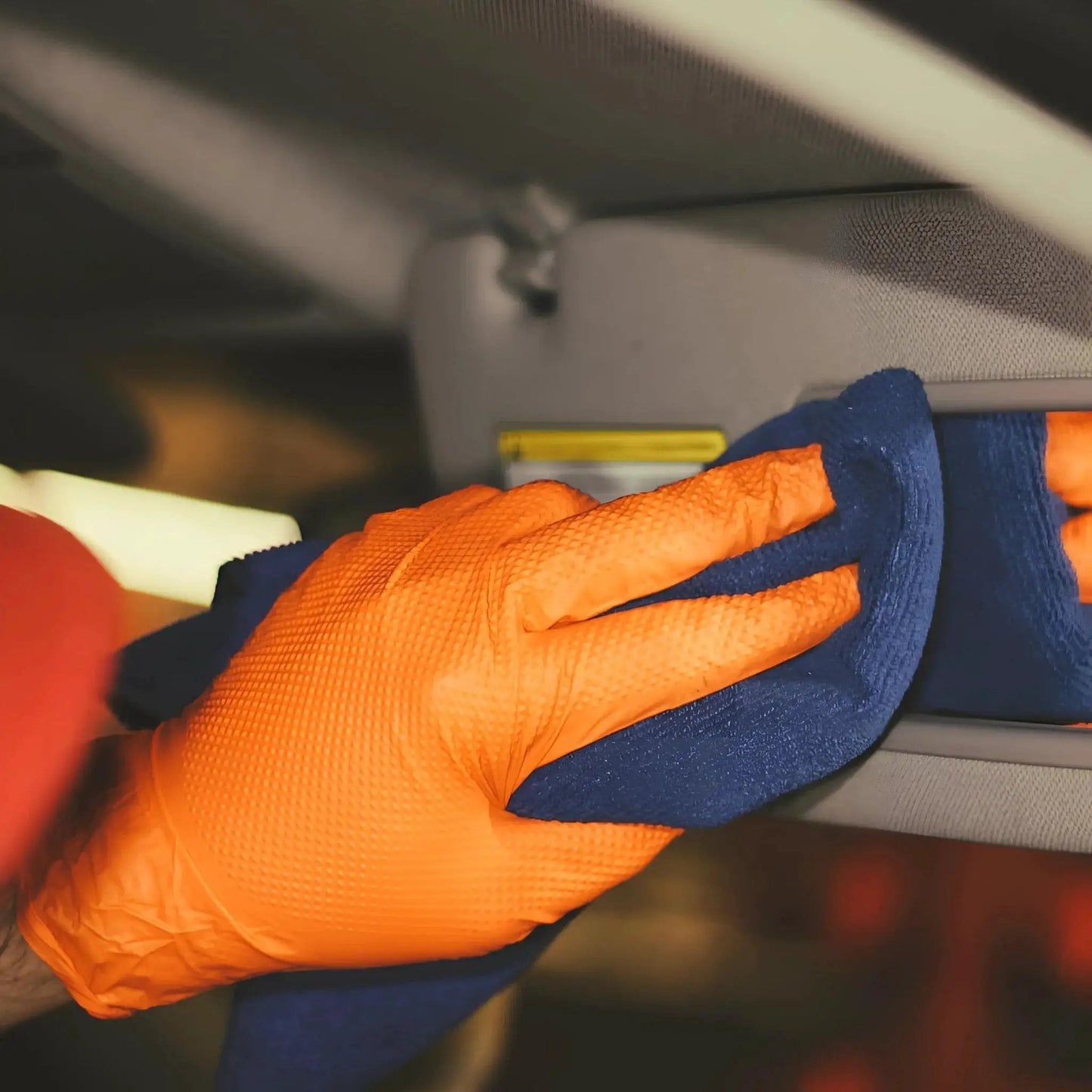 Close-up of hands wearing Heavy Duty Nitrile Gloves 8 Mil Diamond Grip Latex Free Orange XXL 100 Count cleaning car interior