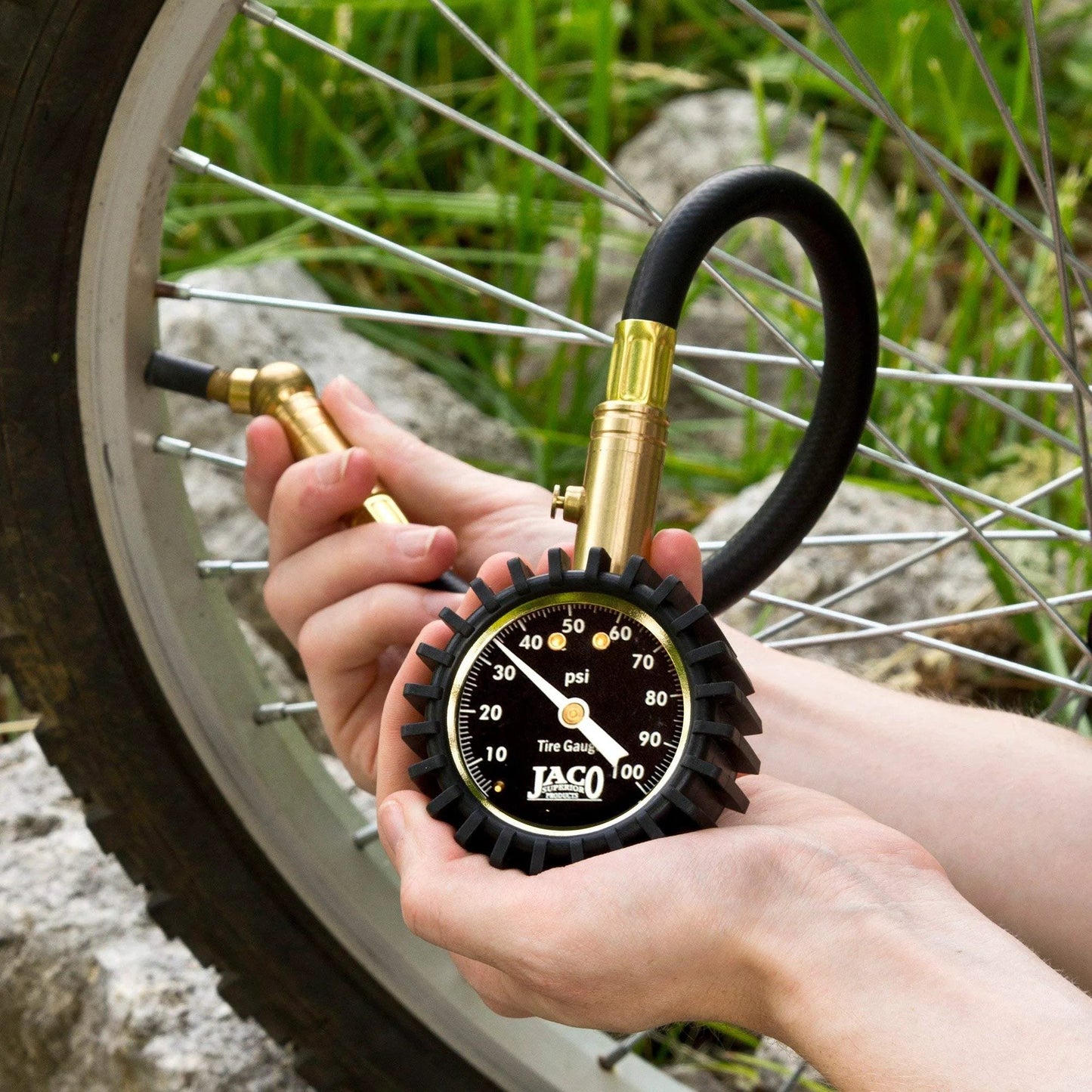 ElitePro Tire Pressure Gauge 100 PSI Mechanic Recommended Battery Free Precision With ANSI Certified Accuracy Plus Or Minus 1.5 Percent Brass Construction Rugged Handheld Tool For Cars Trucks And SUVs being used on a bicycle wheel in a natural setting.