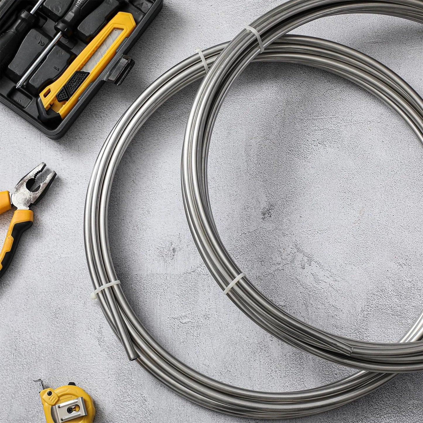 Two Pack 3/8 Inch 304 Stainless Steel Tubing Coils 50 Feet Total 25 Feet Each Heavy Duty Go To Fuel Lines Wort Chillers Automotive Projects And Home Brew MorningRo with tools visible on concrete background.