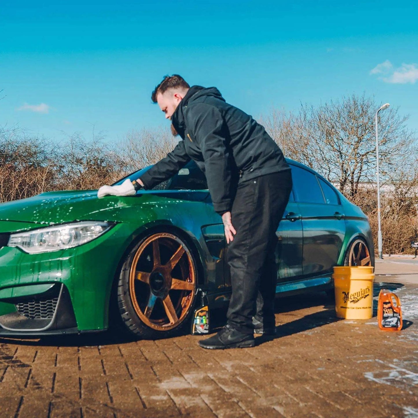 A person using Gold Class Car Wash Shampoo And Conditioner Delivers Pro Results In Foam Cannon Or Bucket Wash While Preserving Wax Protection And A Glossy Finish For All Paint Types 64 Oz Meguiar's on a green car.