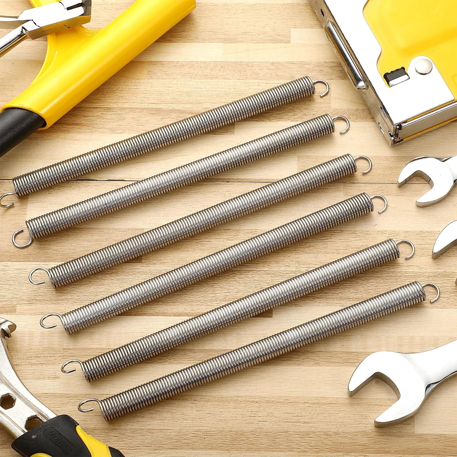 Six Pack Extension Springs 3/8 By 6-1/2 Inch 0.047 Inch Dual Hook Tension Springs For Machinery Repair Industrial Doors And Screens Heavy Duty Equipment Versatile Value Pack Gisafai on a workbench with tools.