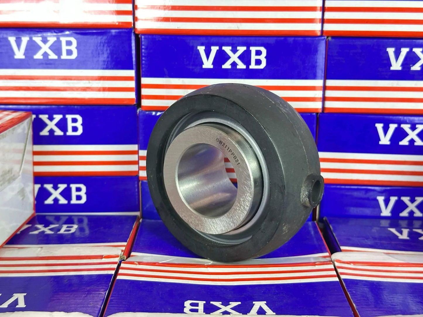 GW211PPB21 Agricultural Heavy Duty Bearing Round Bore Bearing with rubber side view against branded boxes.