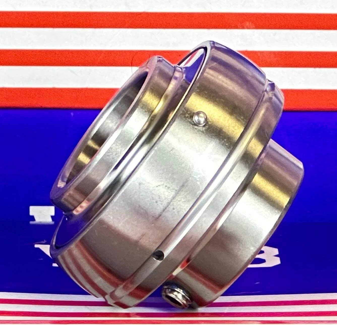 SSUC205-16 Stainless Steel Insert 1" Bore Ball Bearing side view on a red and blue background.