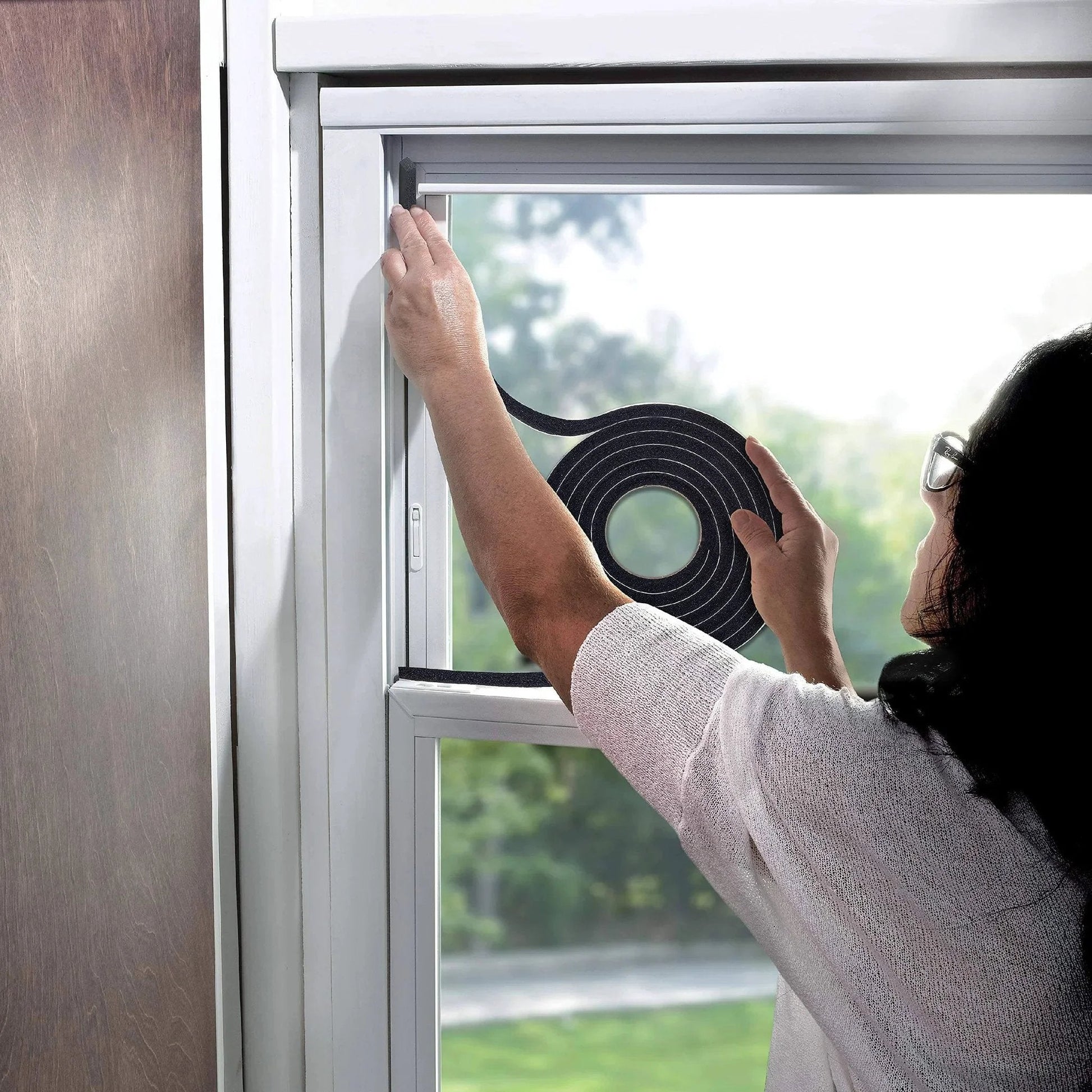 Person applying Self-Stick Rubber Foam Weatherseal, 3/8"W, 3/16"T, Black to window frame to prevent drafts.