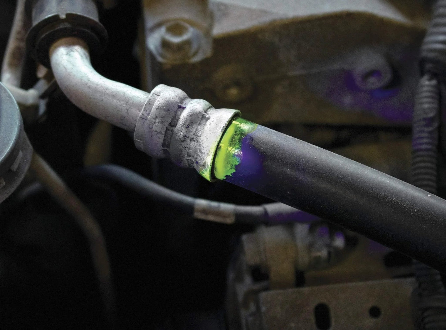 Close-up of a vehicle hose joint with visible UV dye indicating a leak, showcasing vehicle leak detection with the Leak Finder Auto Fluids And Air Conditioning Leak Detection Kit Pro Grade With 1 Oz Dye Injector Syringe UV Light R134A Hose Coupler Made In USA For Quick Easy And Accurate Vehicle Leak Detections For Pro Shops And DIY Maintenance With UV Visibility.