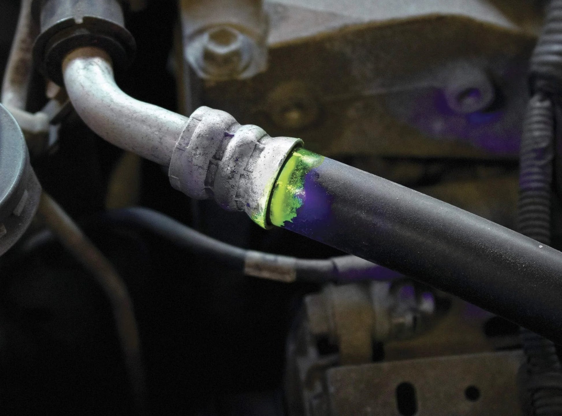 Close-up of a vehicle hose joint with visible UV dye indicating a leak, showcasing vehicle leak detection with the Leak Finder Auto Fluids And Air Conditioning Leak Detection Kit Pro Grade With 1 Oz Dye Injector Syringe UV Light R134A Hose Coupler Made In USA For Quick Easy And Accurate Vehicle Leak Detections For Pro Shops And DIY Maintenance With UV Visibility.