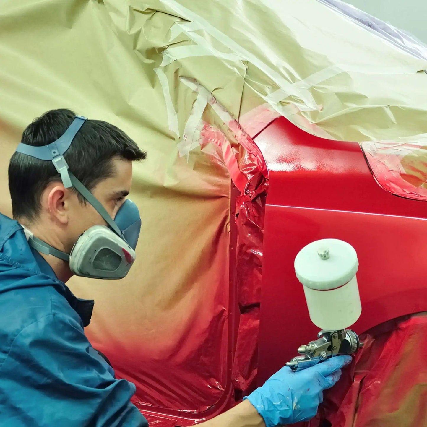 Worker spray painting car part wearing Heavy Duty 8 Mil Nitrile Exam Gloves With Textured Grip Blue 2X-Large, protective mask.