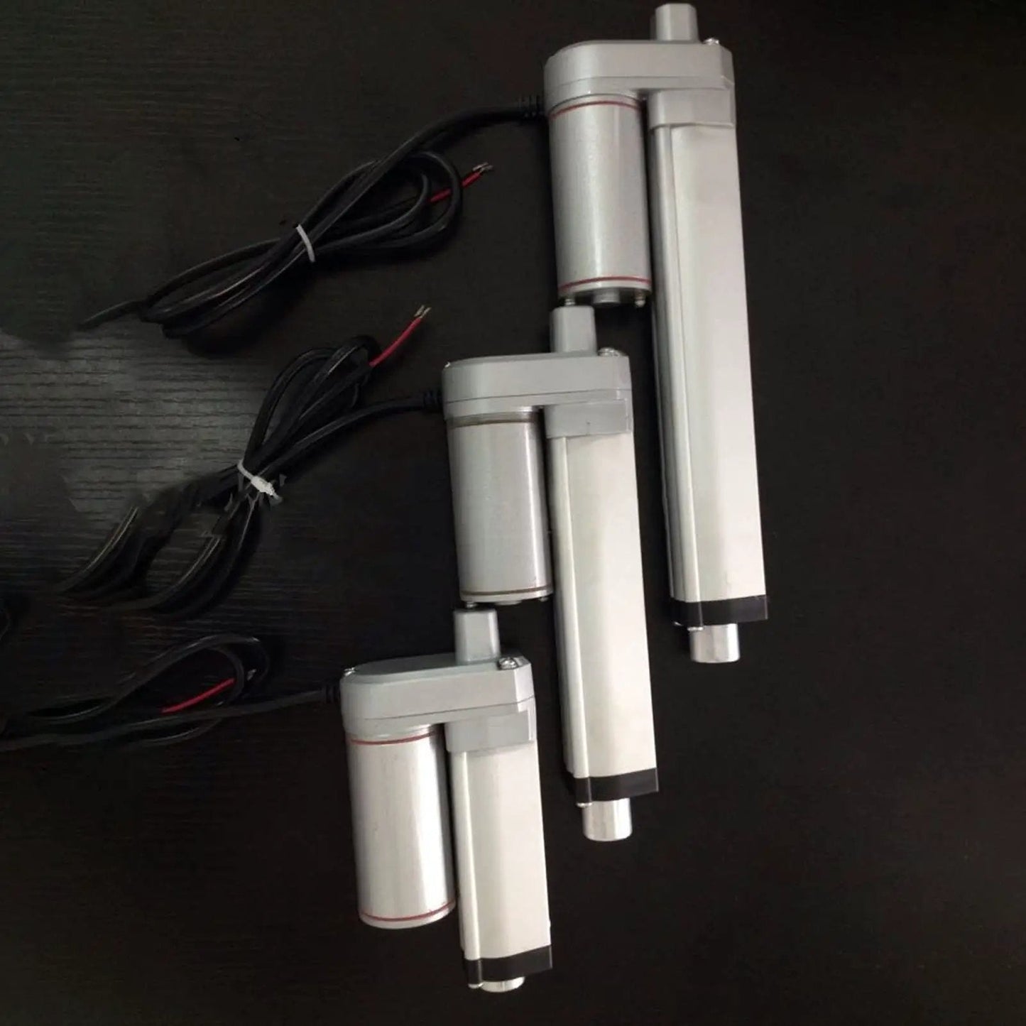 Three 24V DC Linear Actuators With 50mm Stroke 750N Lift IP65 Aluminum Housing showing different sizes, on black background.