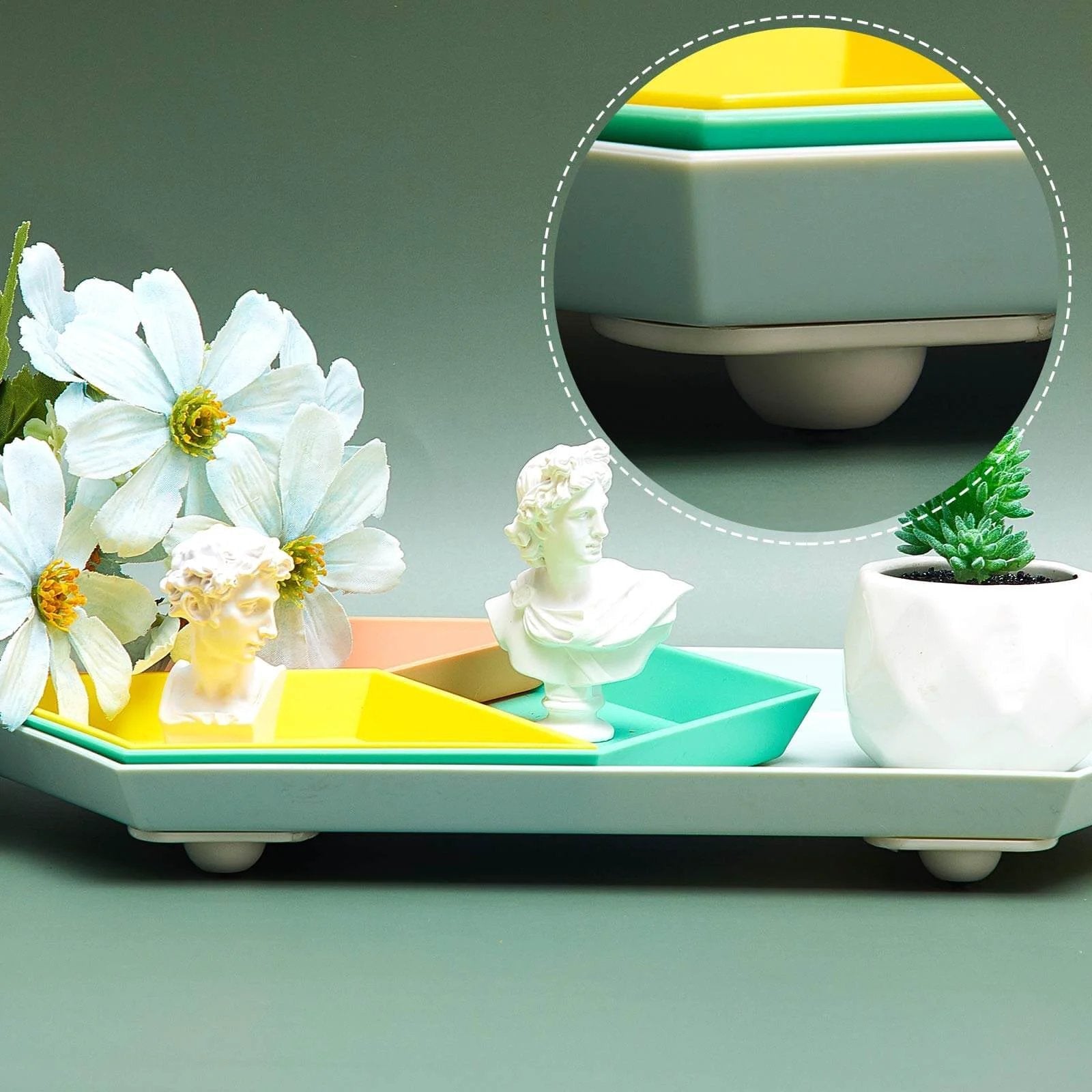Decorative tray with geometric sections, flowers, mini busts, and succulent. Round inset shows close-up of tray's rounded feet.