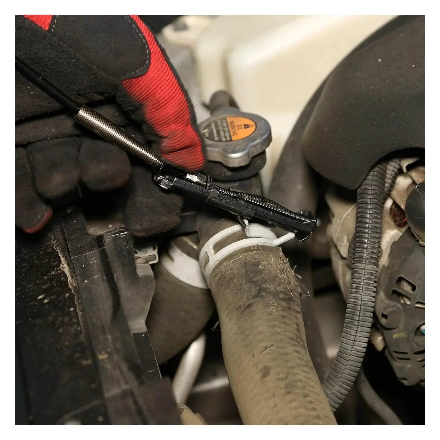 Flexible Hose Clamp Pliers For Automotive Radiator And Heater Hoses Install And Remove Spring Clamps In Hard To Reach Areas Flexible Cable Design With Multi Position Lock For Hands Free Use In Tight Engine Compartments being used to remove a clamp from a hose.