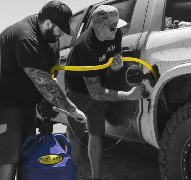 Two people using FLO-FAST Pro Pump, 8GPM, Telescoping Draw Tube, to refuel a vehicle outdoors; portable and durable design.