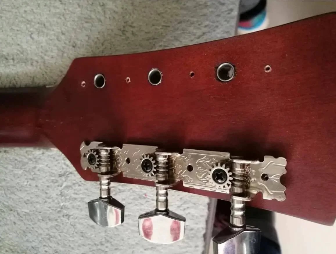 Close-up of guitar headstock with tuning pegs and decorative metal plate on a wooden neck.
