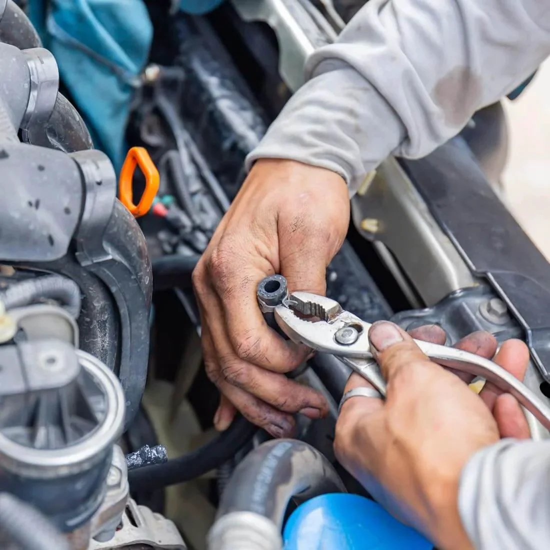 Hands using pliers on spring band type hose clamp in engine, showing installation process in a mechanical setting.