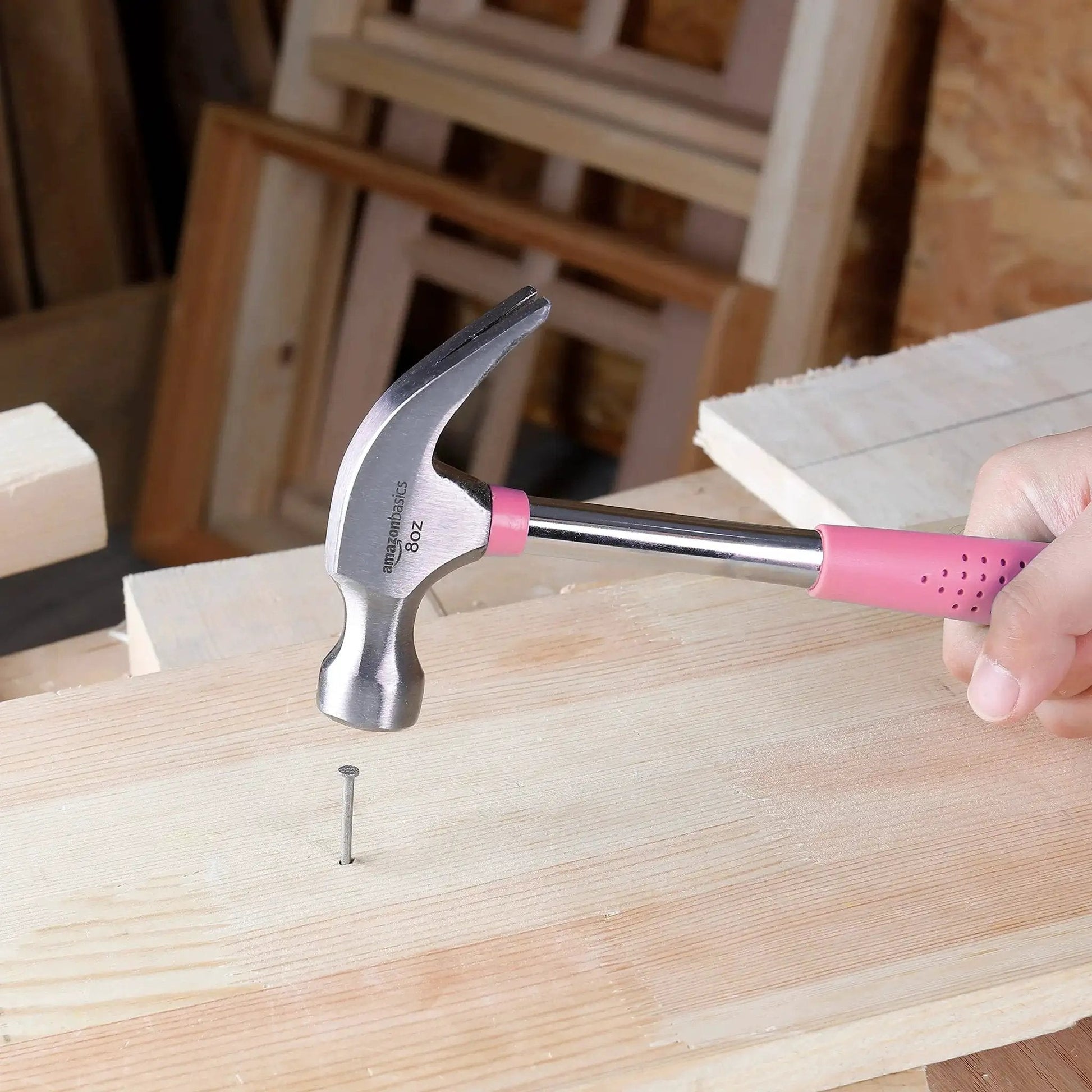 8 oz claw hammer with a shock-absorbing non-slip pink grip used for driving a nail into wood with durable steel head and claw