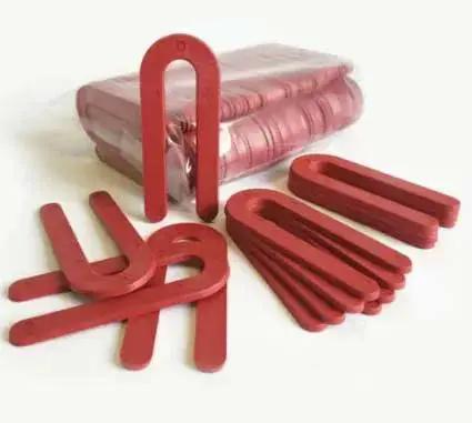 Red Plastic Horseshoe Shims, One Eighth Inch Thick By One And A Half Inch Wide By Three And A Half Inch Long, 100 Pack, displayed spread out