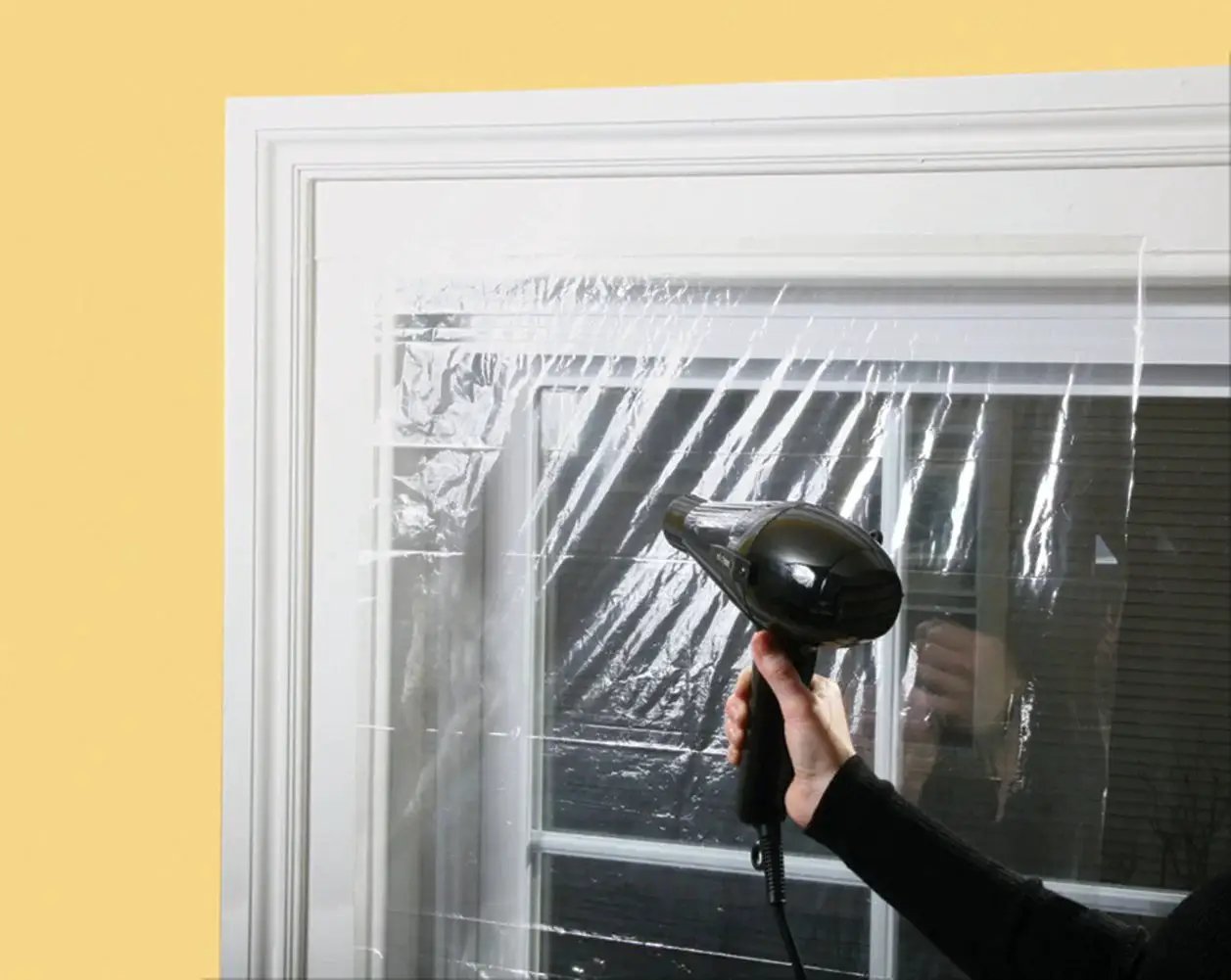 Applying Indoor Window Shrink Kit For 42 To 62 Inch Windows Clear 9 Pack Insulation Film with hairdryer on a window frame
