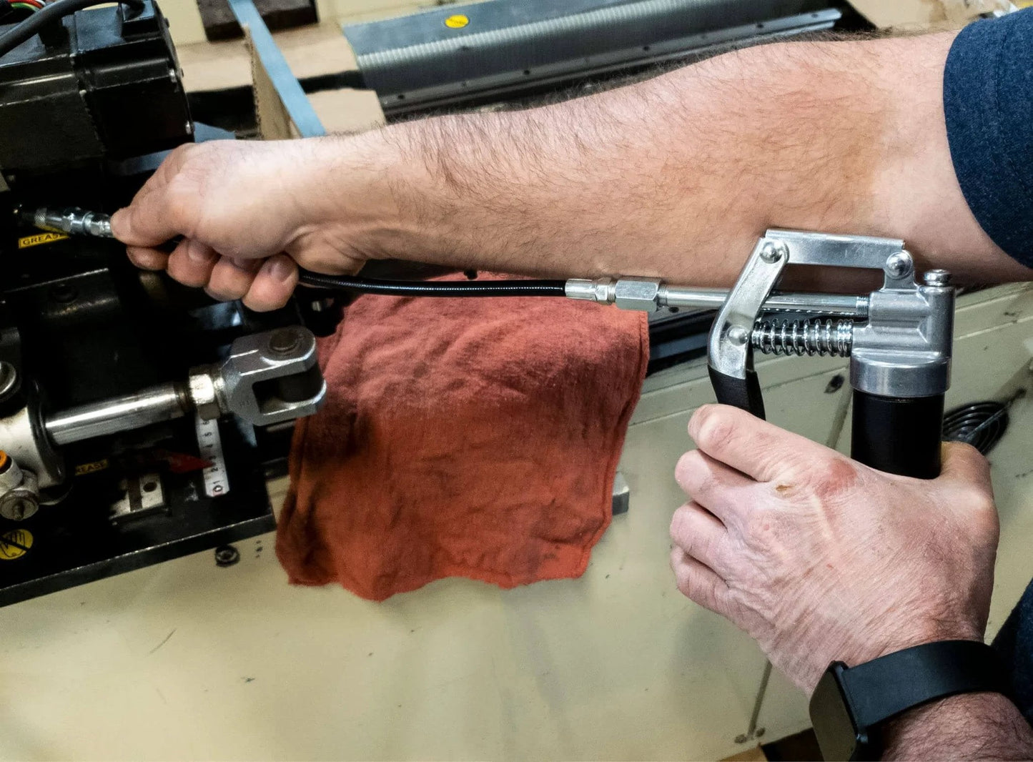 Person using LubriMatic 30-800 Heavy Duty Mini Grease Gun w/ Pipe and Hose, Black/Silver on machinery