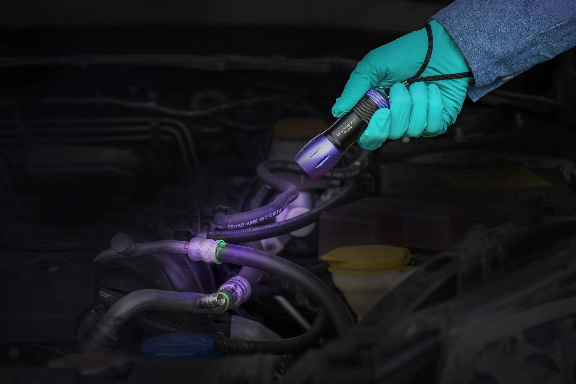 Person using UV light from Leak Finder Auto Fluids And Air Conditioning Leak Detection Kit Pro Grade on vehicle hoses in engine bay.