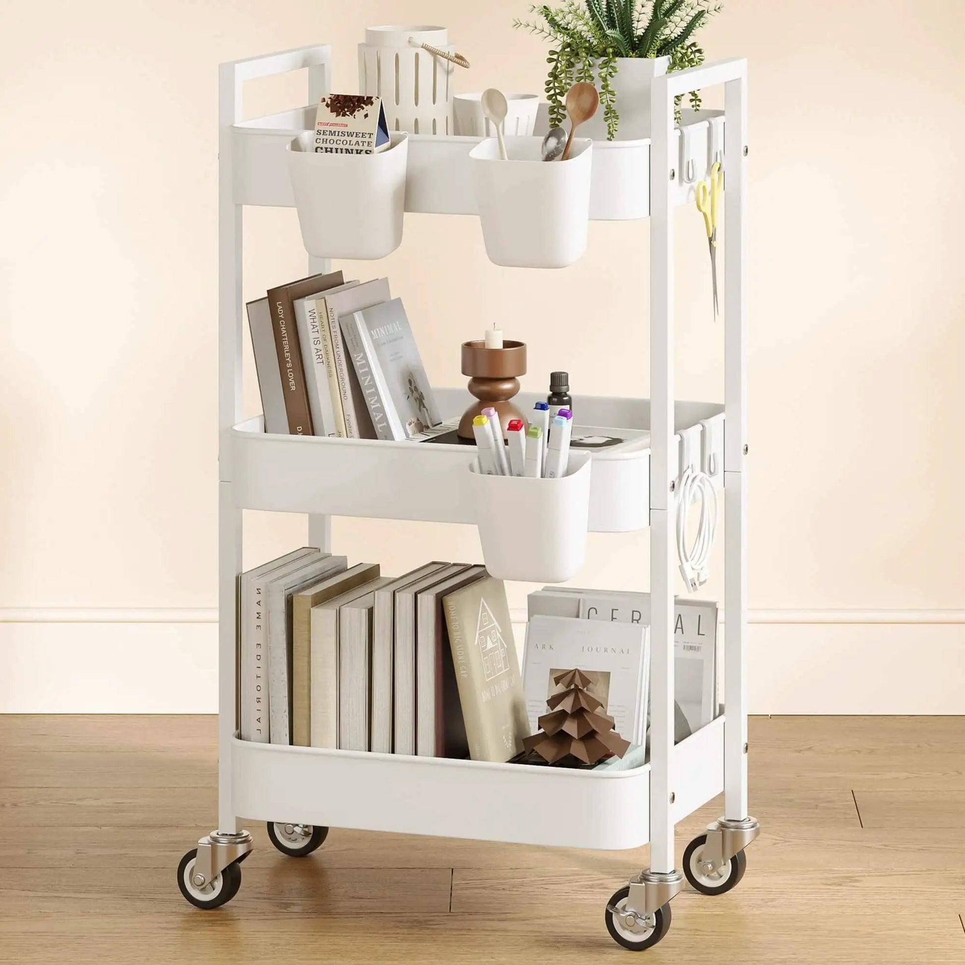 Versatile 3 Tier Rolling Cart With Locking Wheels Hanging Cups And Hooks Heavy Duty Metal Storage Organizer For Kitchen Office Bathroom Craft Room White Perfect For Spices Toiletries Craft Supplies Makeup And More shown loaded with books, plants, and utensils on wooden floor