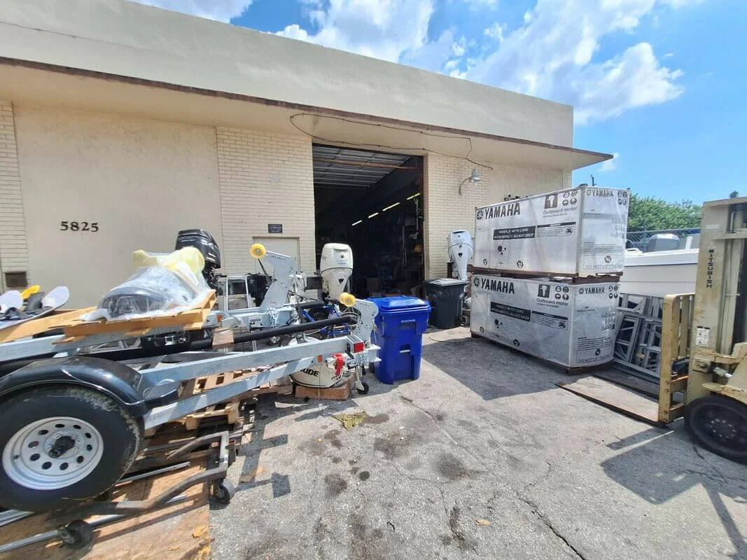 Warehouse exterior with marine equipment and boxed Yamaha motors outside, near open garage door.